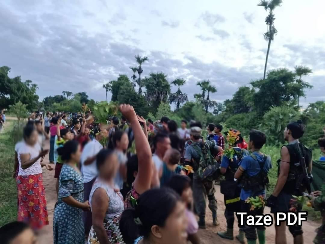 (အောင်ပွဲဖြင့် ပြန်လာသော ပြည်သူ့ကာကွယ်ရေးရဲဘော်များကို ဒေသခံပြည်သူများက သပြေပန်းများဖြင့် ကြိုဆိုနေစဥ်၊ ဓာတ်ပုံ - Taze PDF)