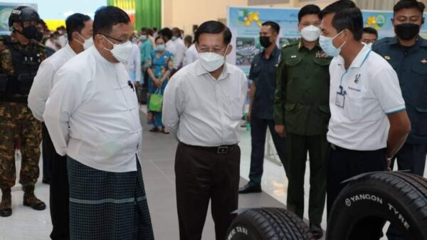 (အာဏာသိမ်းခေါင်းဆောင် မင်းအောင်လှိုင် ​မော်လမြိုင်ခရီးတွင် ပြခန်းလိုက်ကြည့်​နေစဥ် ၎င်း၏​နောက်နားတွင်စစ်​ကောင်စီလုံခြုံ​ရေးတပ်ဖွဲ့ဝင်အချို့​တွေ့ရစဥ်။ (ဓာတ်ပုံ - စစ်​ကောင်စီ)