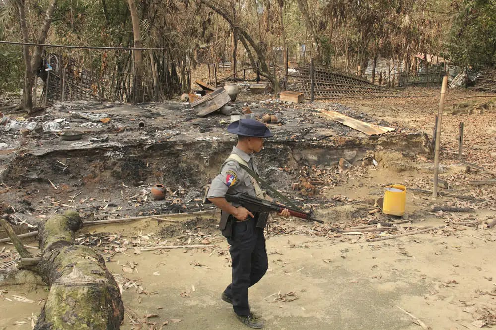 ရခိုင်ပြည်နယ်၊မောင်းတော မြို့နယ်တွင် ၂၀၁၇ ခုနှစ်၌စစ်တပ်နှင့်ရဲများ မီးရှို့ ဖျက်ဆီးခံရသောရိုဟင်ဂျာနေအိမ်ရှေ့မှရဲတစ်ဦး ဖြတ်လျှောက်သွားစဥ်။ဓါတ်ပုံ-AP