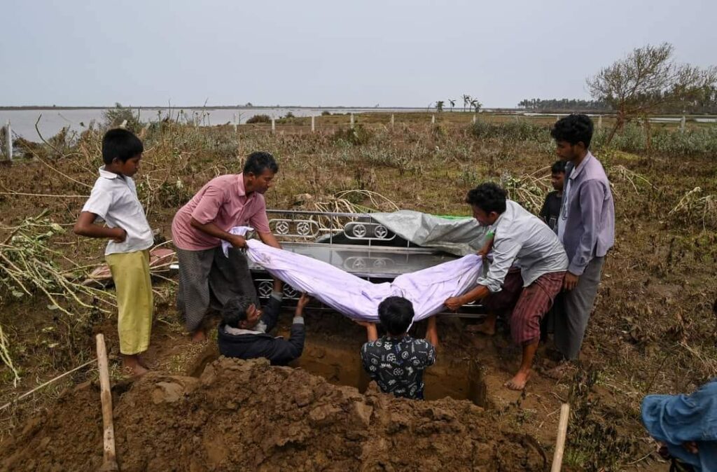 (စစ်တွေမြို့နယ်က မိုခါမုန်တိုင်းဒဏ်ခံခဲ့ရတဲ့ ဂျိုဟင်ဂျာ မွတ်စလင် ဒုက္ခသည်စခန်းတွေနဲ့ ကျေးရွာတွေမှာ မုန်တိုင်းကြောင့် အပျက်အစီးတွေ ၊ သေဆုံးထိခိုက်ပျက်စီးမှုကောက်ယူပြီးတဲ့ရွာစာရင်းနဲ့ သေဆုံးသွားသူတွေရဲ့ နာရေးပြုလုပ်ဖို့ ပြင်ဆင်နေစဥ်။ဓါတ်ပုံ- Getty Images ၊CJ)
