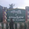 (ကံပိုက်တီ မြို့ဆိုင်းဘုတ် ​ရှေ့တွင် KIA တပ်ဖွဲ့ဝင်တဦး ။ဓါတ်ပုံ-​ပေးပို့)