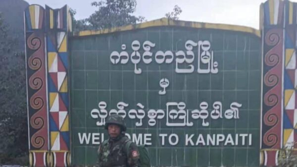 (ကံပိုက်တီ မြို့ဆိုင်းဘုတ် ​ရှေ့တွင် KIA တပ်ဖွဲ့ဝင်တဦး ။ဓါတ်ပုံ-​ပေးပို့)
